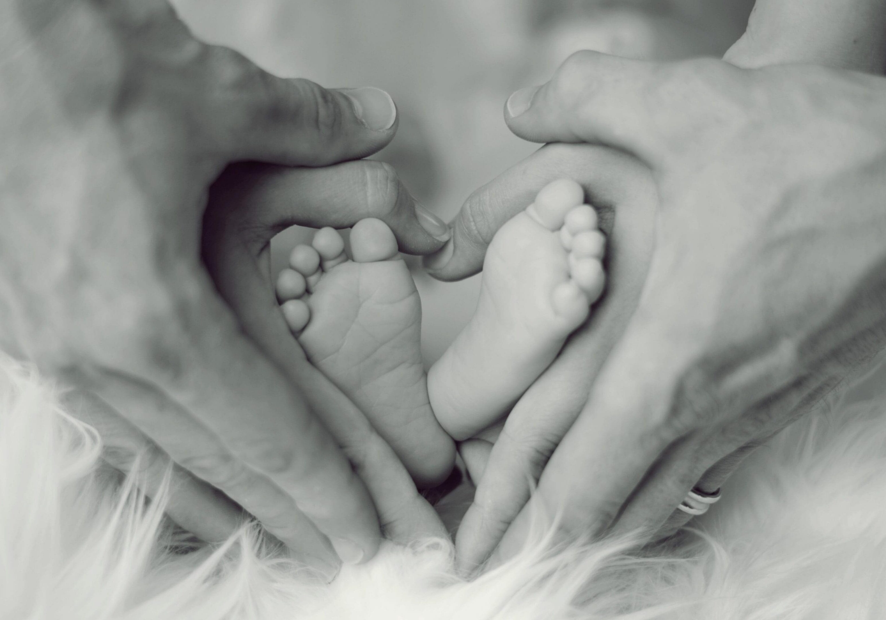 Newborn infant cradled in a parent's hands, illustrating rachamim — the Hebrew word for womb-deep compassion in Isaiah 49