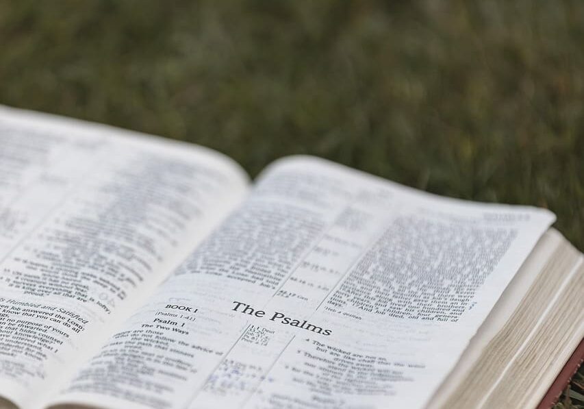 Open Bible on a wooden table with soft light, who is Jesus really